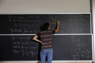 photo of person writing on chalkboard, back turned