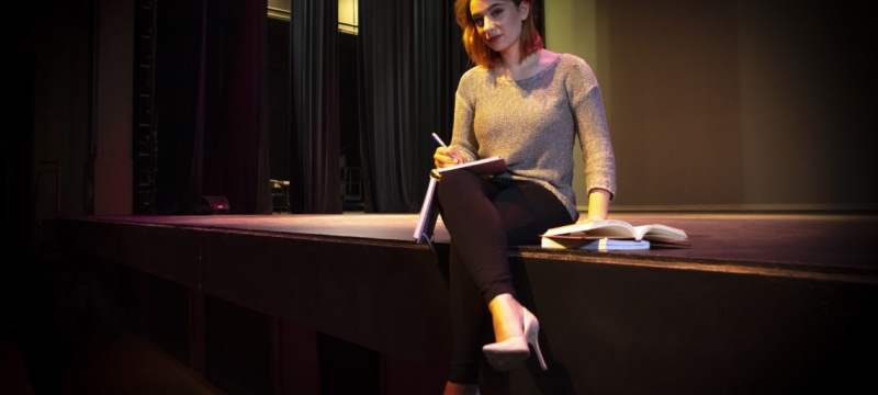 photo of woman sitting on stage with book and pen