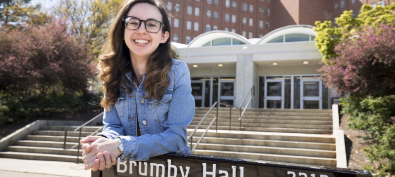 photo of woman leaning on dorm sign