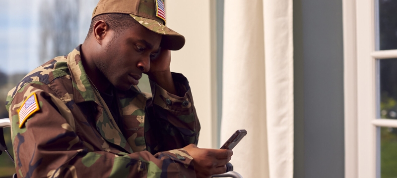 photo of man seated looking at cell phone
