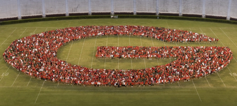 photo of people forming the letter G on a stadium grass field