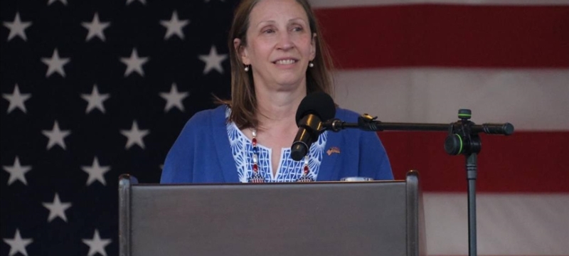 photo of woman at podium, American flag in background