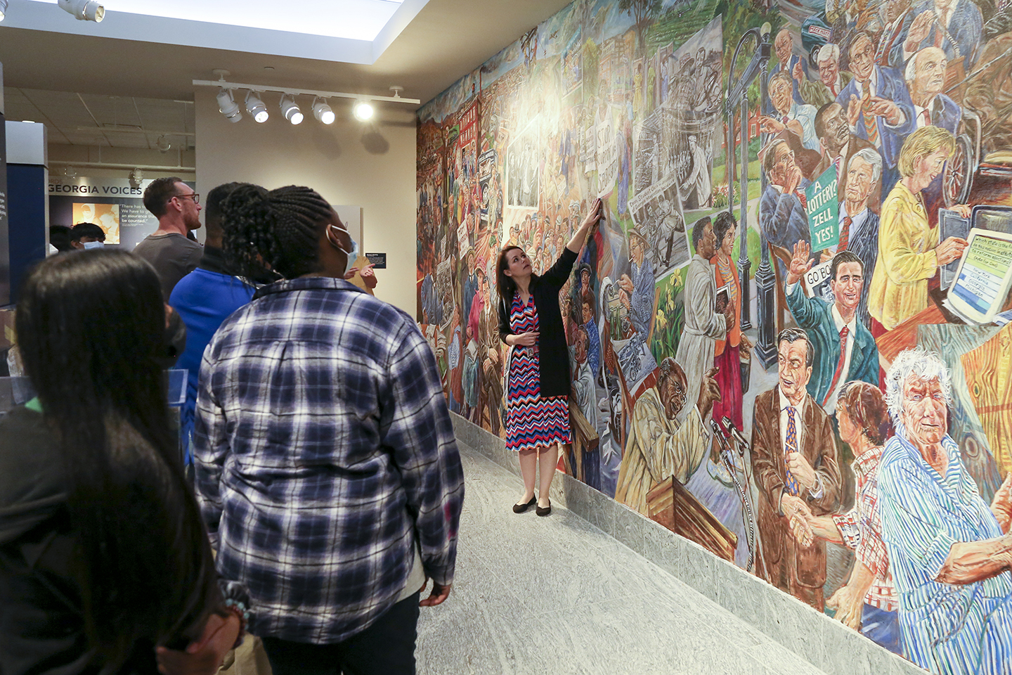photo of students, with mural and woman pointing