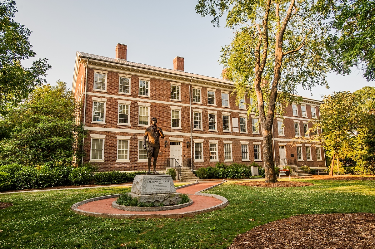 Photo of story building on campus, with statue in front, day.