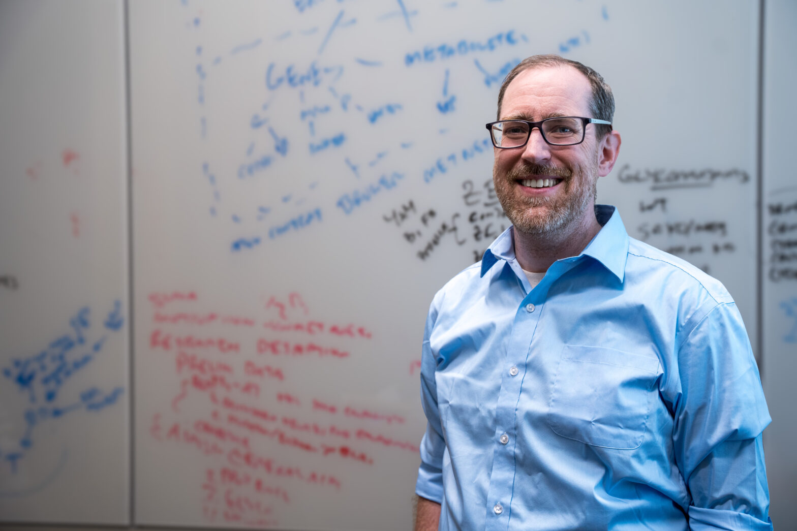 photo of man, dry erase board with blue, black and red writing in background