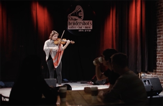 still photo of woman playing violin on a club stage