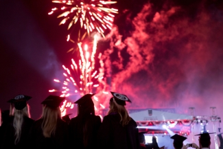 photo of people in caps and gowns, with fireworks in background