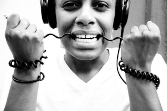 black and white photo of woman wearing headphones with the cord in her teeth