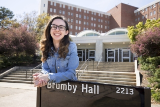 photo of woman leaning on dorm sign