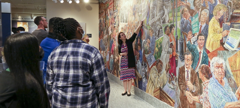photo of students, with mural and woman pointing