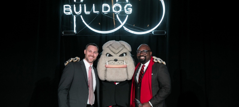 photo of two men with Hairy Dawg mascot and Neon sign
