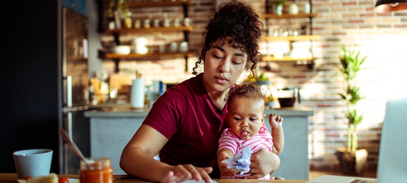 photo of woman holding baby, with laptop in kitchen