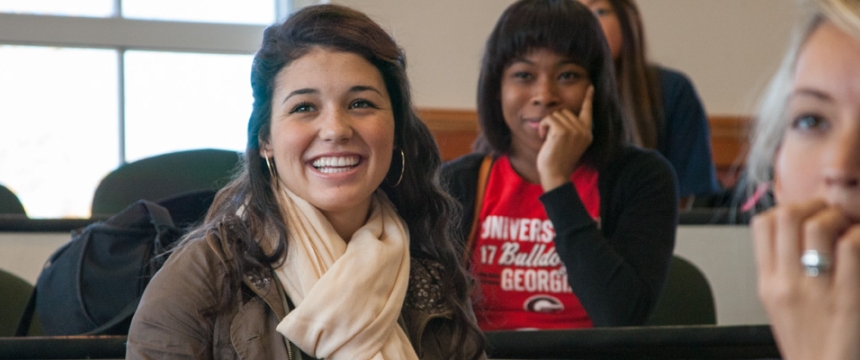 Three diverse female students grin as they listen to Daleah Goodwin's lecture in a women's studies class in the Miller Learning Center 
