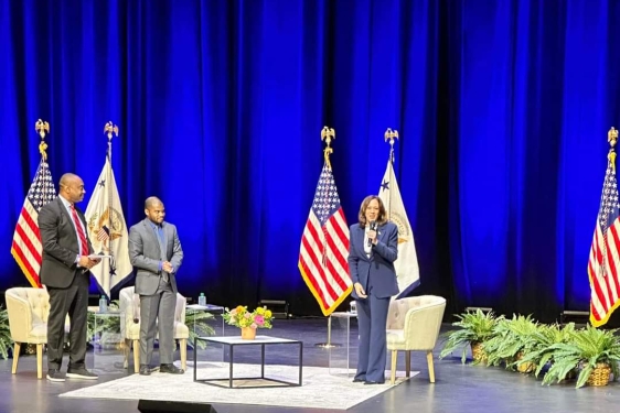 photo of three people on stage, with flags and chairs