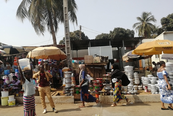 Photo of outdoor marketplace with goods, umbrellas, people and palm trees