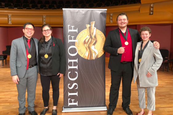 photo of four people with medals and banner in performance hall