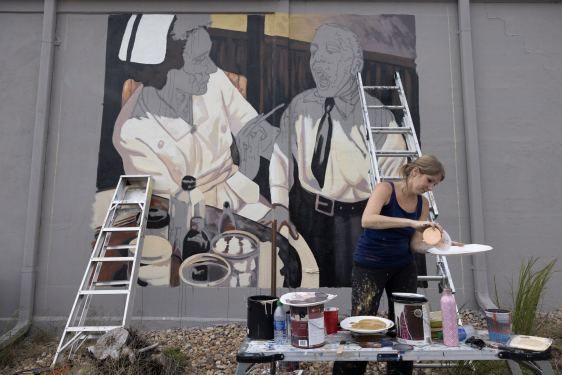 photo of woman mixing paint with mural, ladders, and paint cans