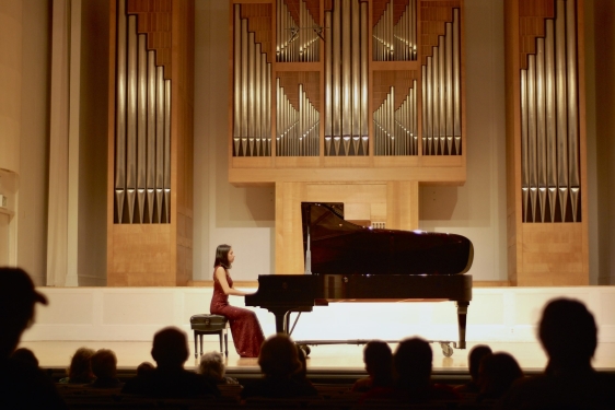 photo of woman in piano performance, with audience silhouette foreground