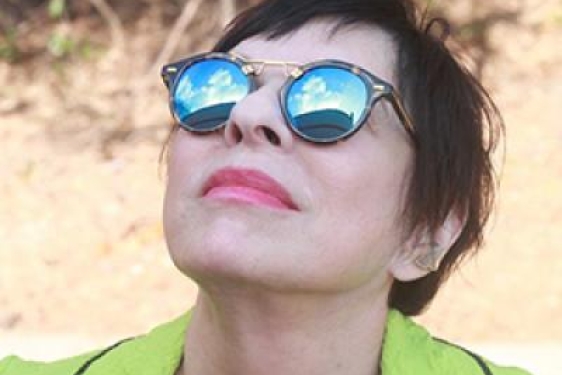 photo of woman looking up, with sunglasses reflecting sky