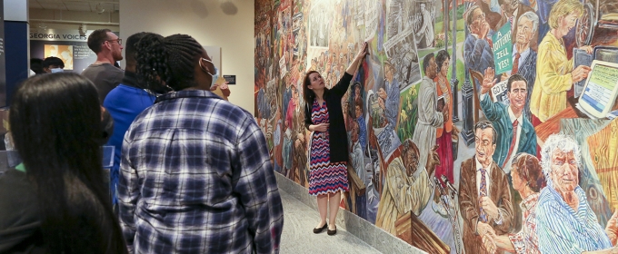 photo of students, with mural and woman pointing