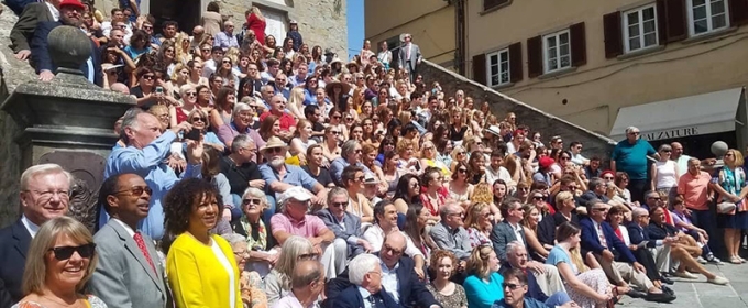 photo of a large group seated on sunny steps of a medieval palace.