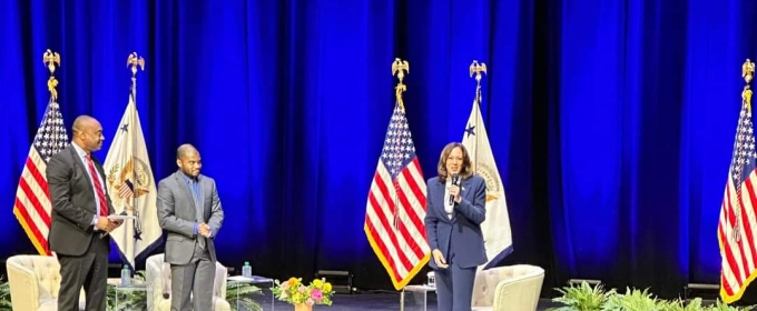 photo of three people on stage, with flags and chairs