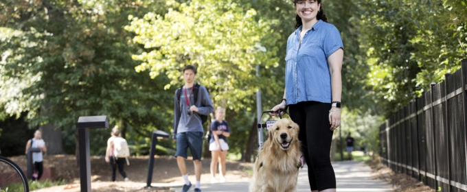 outdoor photo of woman with service dog on sidewalk and other pedestrians.